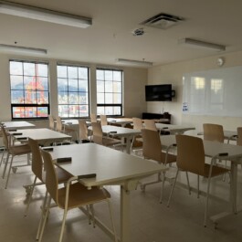 Bright classroom with white walls, window views of the mountains, a whiteboard, large white desks, and wooden chairs. Vancouver Japanese Language School & Japanese Hall